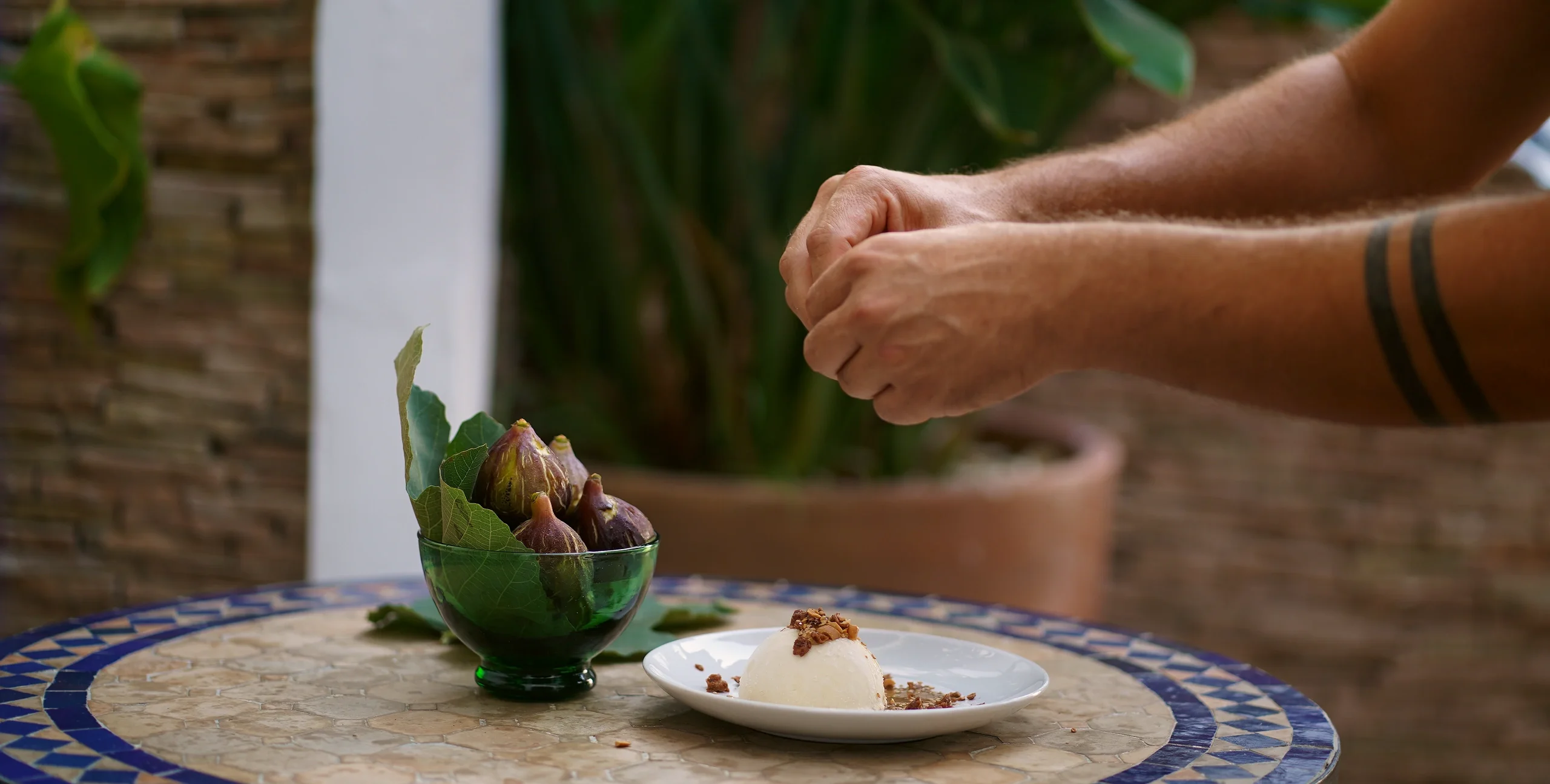 Bowl of fresh figs beside a plated dessert on a tiled table
